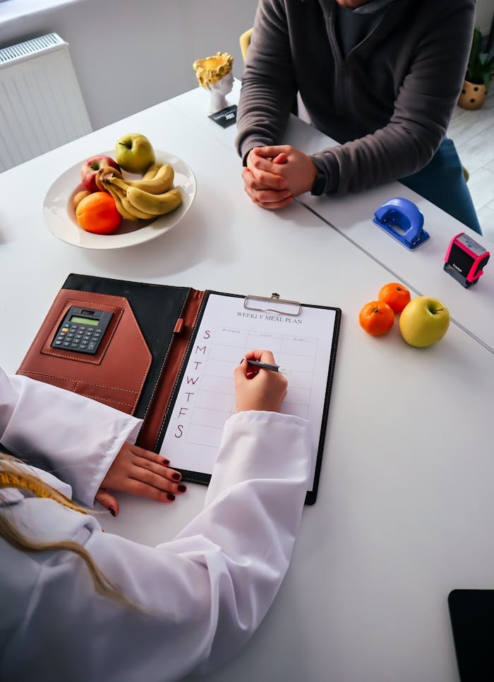 hero-img-02 A nutritionist writes a weekly meal plan for a client in an office setting, surrounded by fresh fruits.