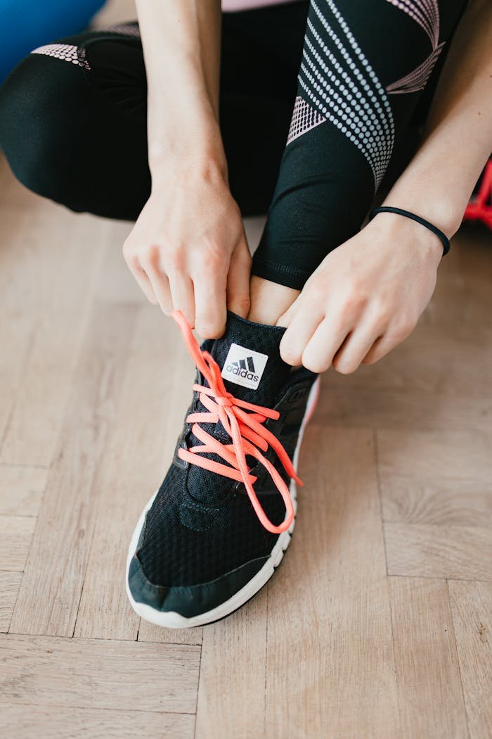 services-01 From above young anonymous female athlete in leggings adjusting sneakers while sitting on wooden floor in modern fitness studio and preparing for training