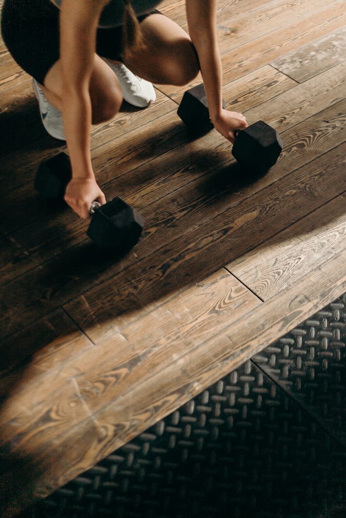 services-img Female gym-goer in action with dumbbells on wooden floor, ready to lift.