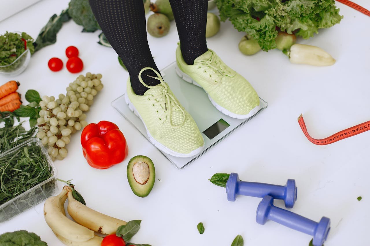 services-02 Person standing on scales surrounded by fresh produce and fitness equipment symbolizing a balanced lifestyle.
