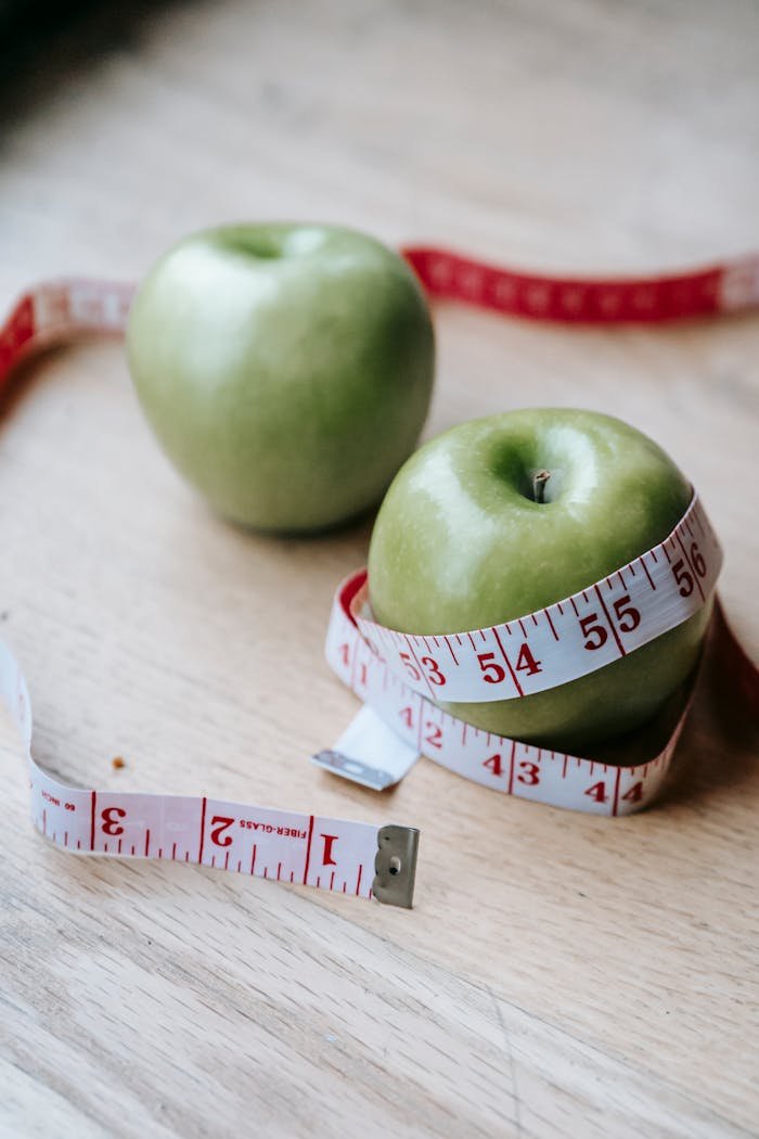 contact-img From above of healthy ripe green apples with measuring tape placed on wooden table in light room on blurred background
