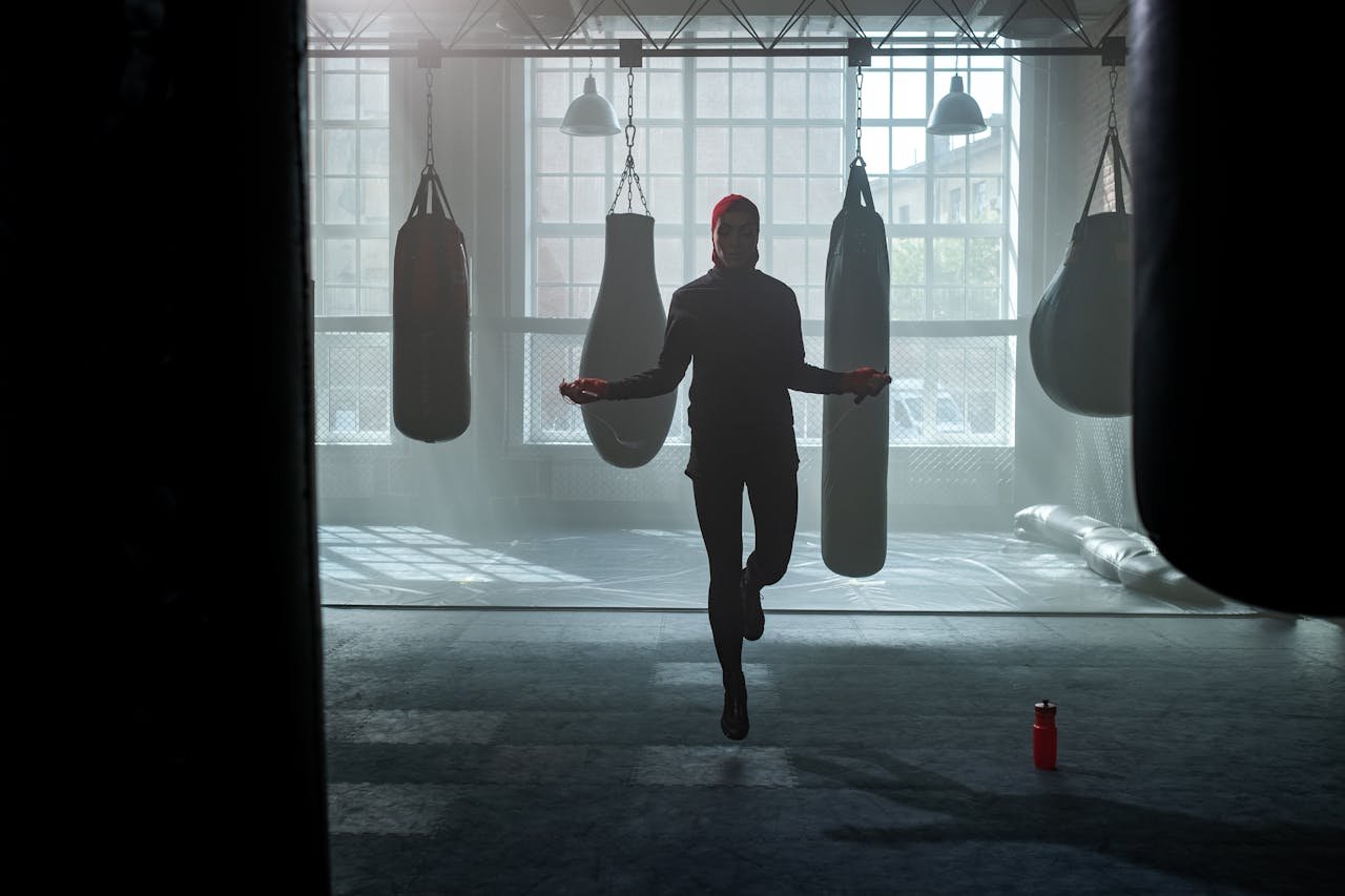 services-04 A woman exercises by jumping rope in a gym filled with punching bags.